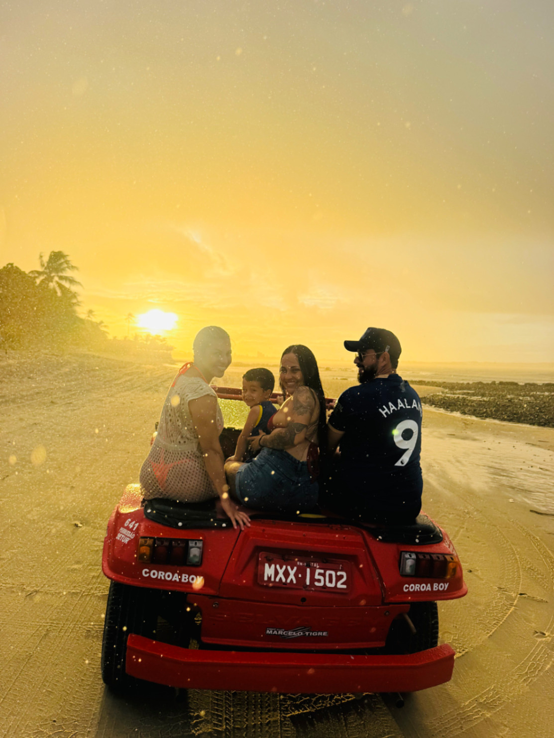 Família em buggy vermelho durante o pôr do sol na praia