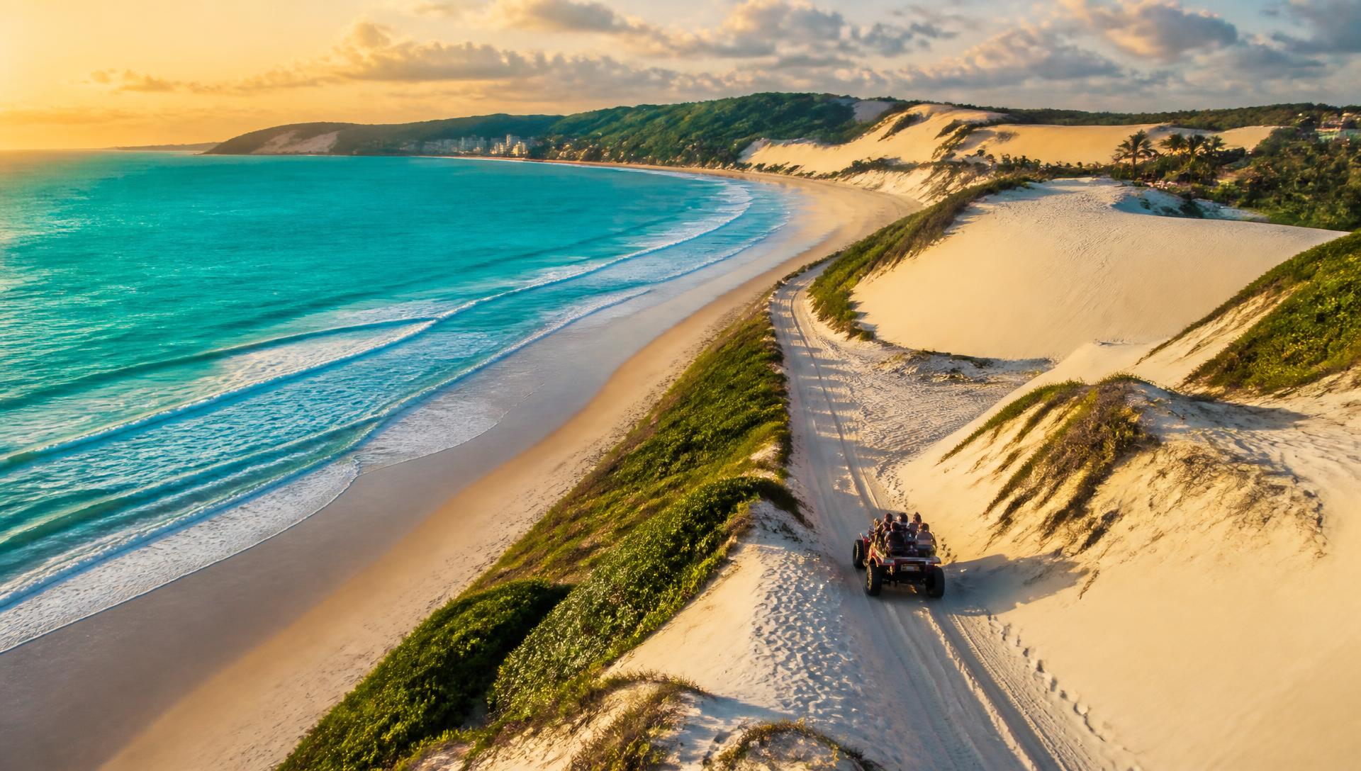 Buggy percorrendo as dunas de Natal ao pôr do sol com o mar ao fundo